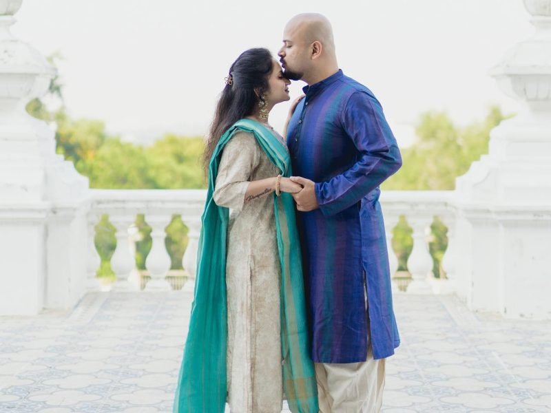 Bride and groom in casual Indian wear at white palace, groom kissing bride’s forehead